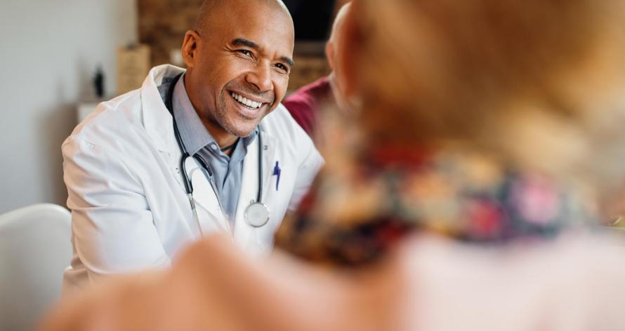 Happy African American doctor talking to senior couple during home visit.
